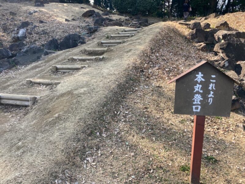 土の斜面に作られた階段と案内板本丸登山口