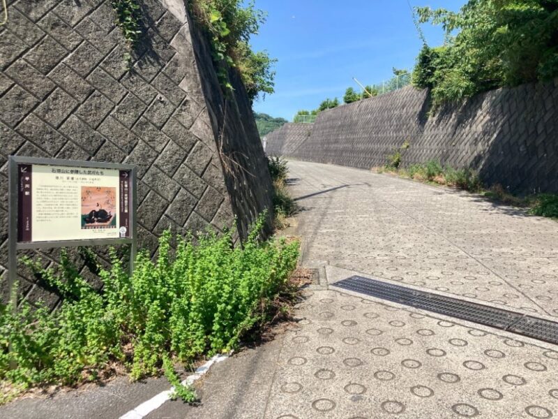 石垣のある坂道の風景案内板と草が生い茂っている